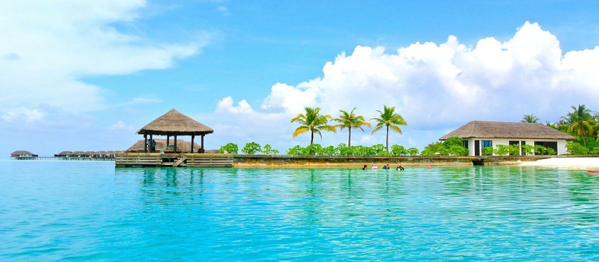 Tropical island resort with a thatched gazebo on a wooden pier extending over turquoise lagoon.